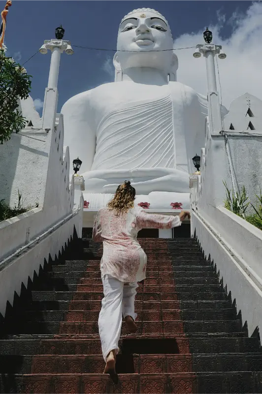 Tourist climbing steps towards the giant Bahirawakanda Buddha Statue in Kandy, Sri Lanka, on a sunny day.